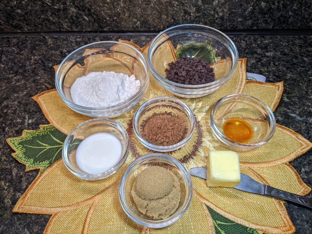 All of the ingredients for edible cookie dough: flour, milk, cocoa powder, brown sugar, vanilla extract, butter, and chocolate chips.