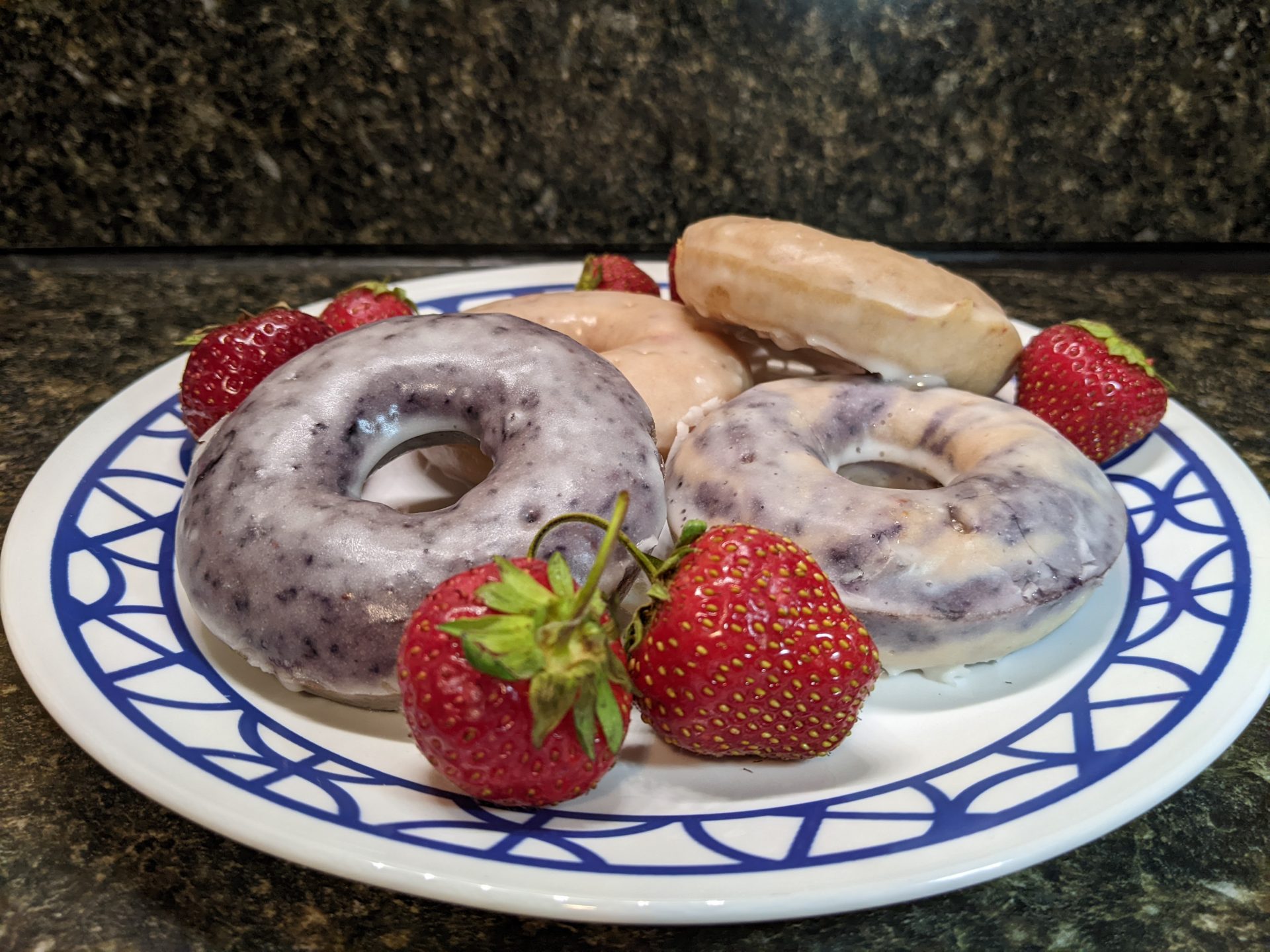 A plate of several berry donuts, surrounded by strawberries.