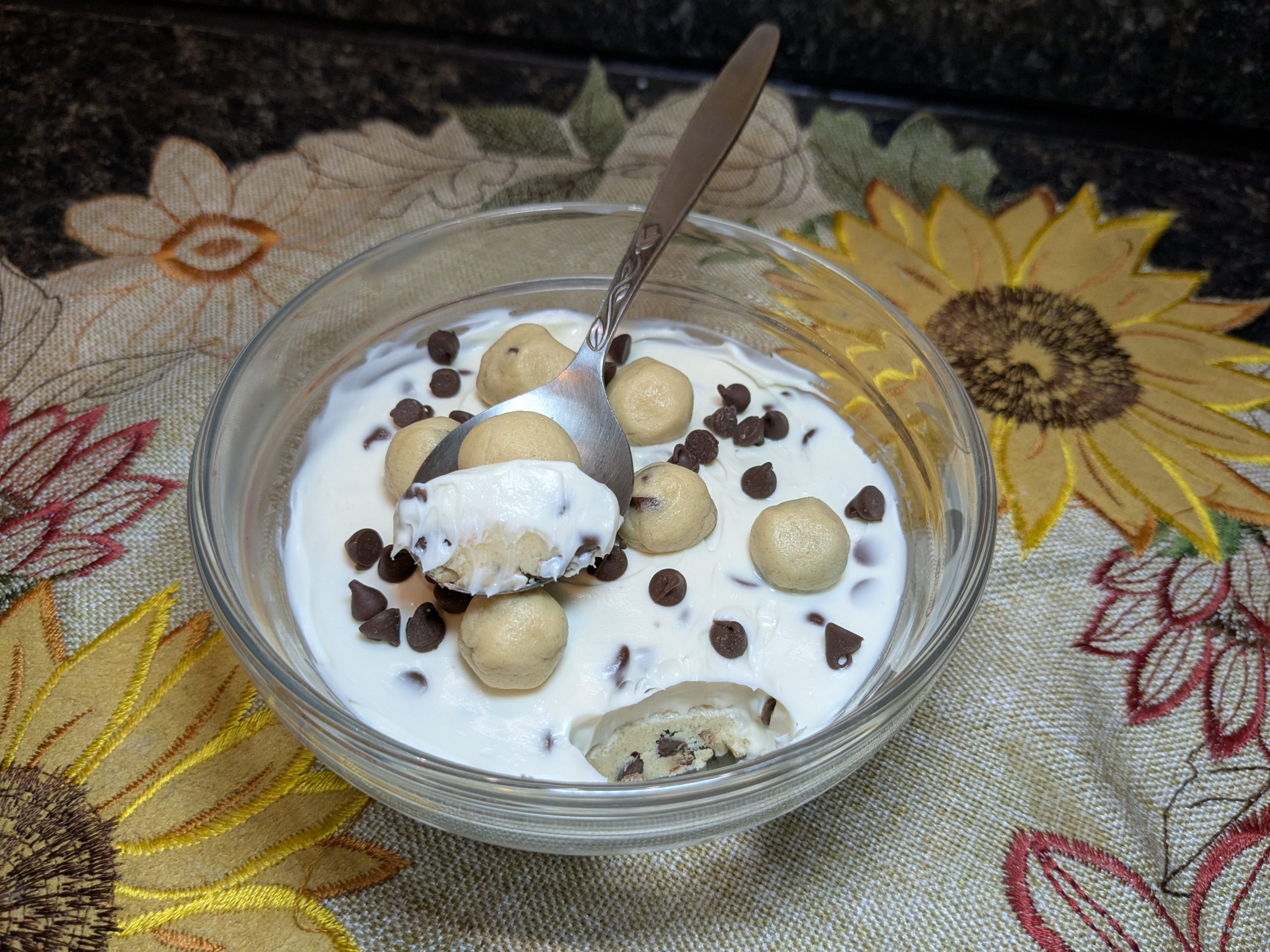 A small glass bowl with edible cookie dough and a layer of cheesecake cream on top.