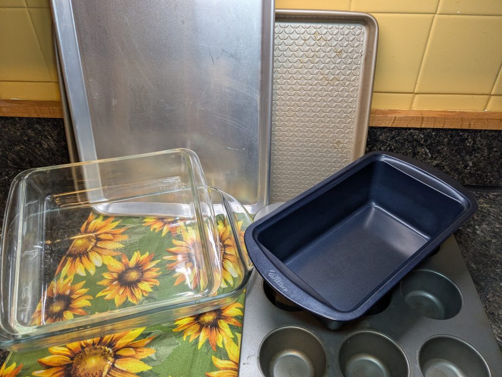 A photo of various baking dishes, including two cookie sheets, two glass baking dishes, a loaf pan, and a muffin tin.