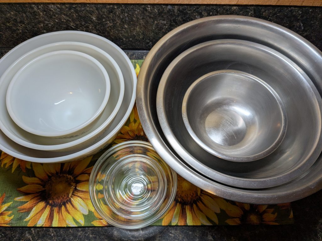 A photo of three sets of bowls; three Pyrex mixing bowls, three steel mixing bowls, and three smaller glass prep bowls.