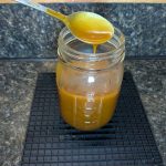 A half-full pint jar of salted caramel sauce, a spoonful streaming into the jar from above.