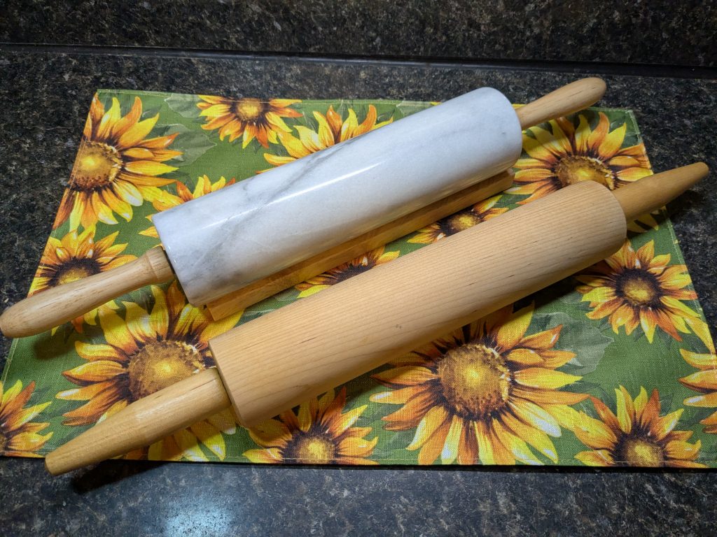 A photo of two rolling pins, one made of light marble and one made of wood.