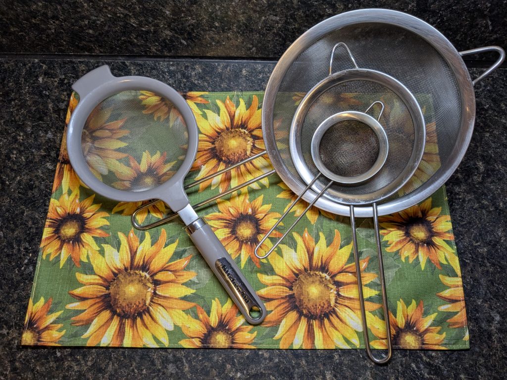 A photo of four sieves of various sizes, three in a wire set and one Kitchenaid sieve with a finer mesh.