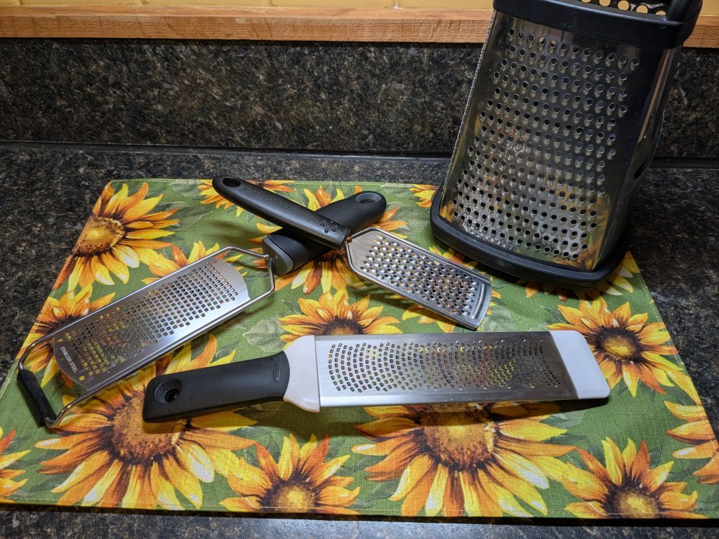 A photo of two zesters, a handheld grater, and a box grater.